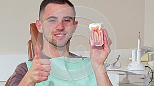 Handsome young man smiling to the camera holding dental mold at the clinic