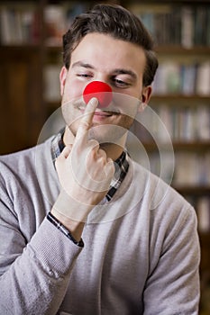 Handsome young man smiling and touching red clown nose