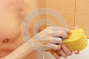 Handsome young man soaping yellow sponge with soap