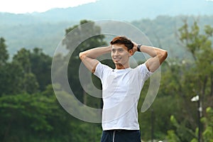 Handsome young man in sportswear warming up before sports training outdoors with beautiful nature view in background