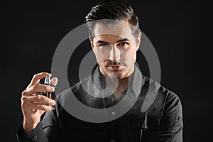 Handsome young man spraying perfume on background