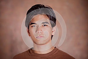 Handsome young man standing against brown background with serious expression