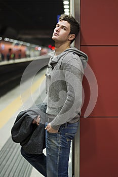 Handsome young man standing against wall in train or subway station