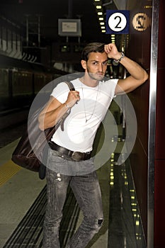 Handsome young man standing against wall in train or subway station