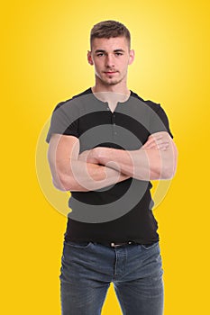 Handsome young man standing with arms folded over yellow background