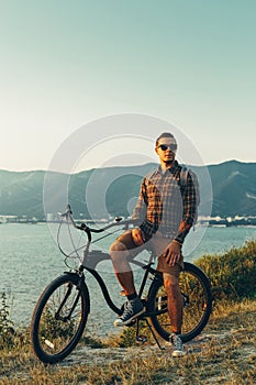 Handsome Young Man Standing With Bike On Coast And Enjoying View of Nature Sunset Vacation Traveling Relaxation Resting Concept