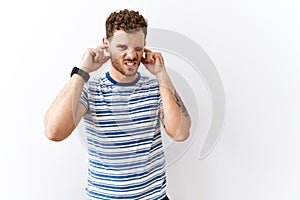 Handsome young man standing over isolated background covering ears with fingers with annoyed expression for the noise of loud