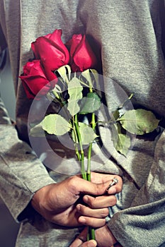 Handsome young man  standing with red roses behind the back on blurred happiness smiling girlfriend background..Man buys flowers