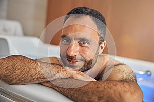 Handsome young man with stubble relaxing in bathtub