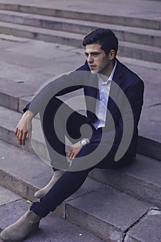 Handsome young man with styled hair. The man is sitting on the steps.