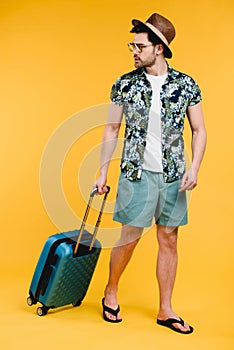 handsome young man in summer outfit holding suitcase and looking away