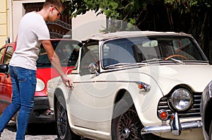 Handsome young man in sunglasses standing in urban city street next to an old retro car. A guy opening and entering old timer car.