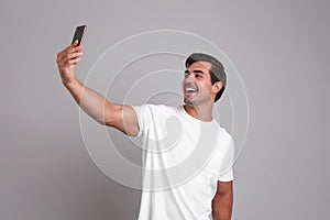Handsome young man taking selfie with smartphone on background