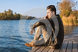 Handsome young man talking on his phone by the water