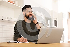 Handsome young man talking on phone while working at table