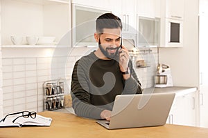 Handsome young man talking on phone while working at table