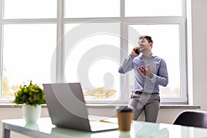 Handsome young man talking on smart phone and using computer while working in the office