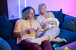 Handsome young man teaching how to play the video games to his girlfriend, on the couch, concept about home