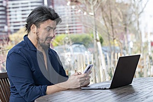 Handsome young man texting on phone in front of his laptop