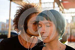 Handsome young man touches  his girlfriend`s hair with his nose. Couple in love. Lovers listen to music together at sunset