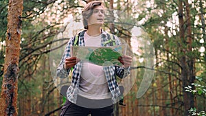 Handsome young man traveler is walking in forest then standing and looking at map searching for right way then going