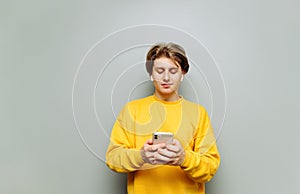 Handsome young man uses a smartphone on a gray wall background and listens to music. guy in the wireless headphones uses the