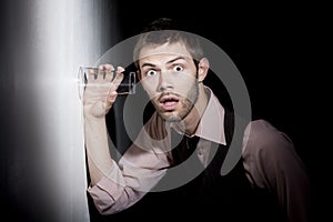 Handsome young man using glass to eavesdrop
