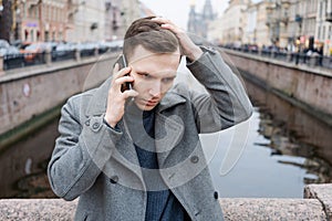 Handsome young man using mobile phone, wearing an elegant gray coat, stands