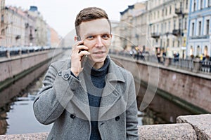 Handsome young man using mobile phone, wearing an elegant gray coat, stands