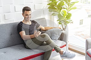 Handsome young man using mobile on sofa. Wireless network connection for modern life concept