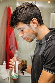 Handsome young man using mouthwash, in bathroom