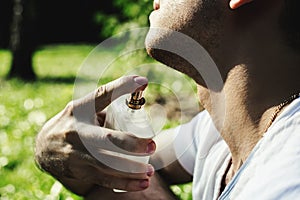 Handsome young man using perfume on green background