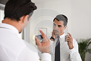 Handsome young man using perfume near mirror