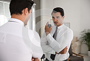 Handsome young man using perfume near mirror