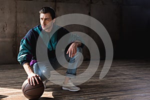 handsome young man in vintage windcheater with basketball ball sitting squats photo