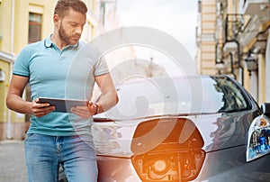 Handsome young man watching his car charging