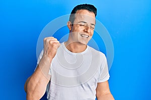 Handsome young man wearing casual white t shirt celebrating surprised and amazed for success with arms raised and eyes closed