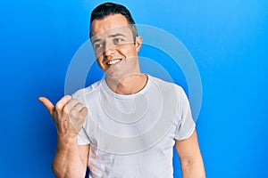 Handsome young man wearing casual white t shirt pointing thumb up to the side smiling happy with open mouth