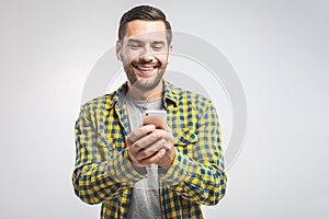 Handsome young man wearing headphones and holding mobile phone while standing against grey wall