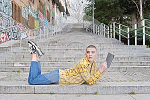 Handsome young man wearing make up, reading a book lying on stairs with his feet up