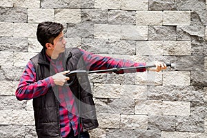 Handsome young man wearing square pattern red holding high pressure water gun, pointing towards grey brick wall photo