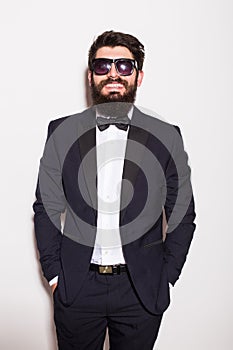 Handsome young man wearing suit and glasses keeping hands in pockets and looking at camera
