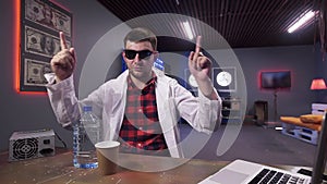 Handsome young man wearing white lab coat sits behind desk with plastic bottle