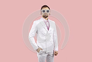 Handsome young man wearing white suit, sunglasses and headphones listening to music