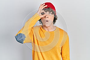 Handsome young man wearing wool hat doing ok gesture shocked with surprised face, eye looking through fingers