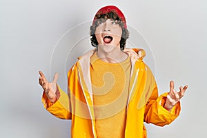 Handsome young man wearing yellow raincoat crazy and mad shouting and yelling with aggressive expression and arms raised