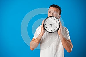 Handsome young man in white t-shirt posing with clock against blue background