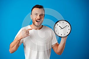 Handsome young man in white t-shirt posing with clock against blue background