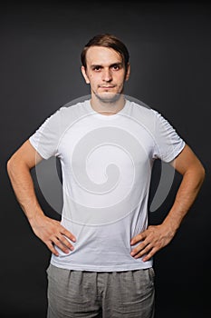 A handsome young man in a white t-shirt stands on a gray background. mockup