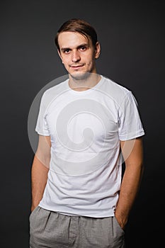 A handsome young man in a white t-shirt stands on a gray background. mockup